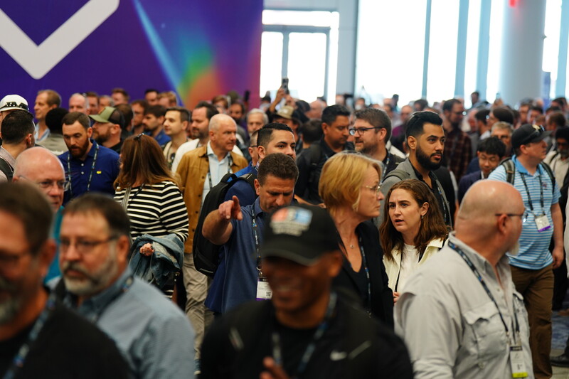 Large indoor crowd of people at a conference or convention event with purple and rainbow lighting.