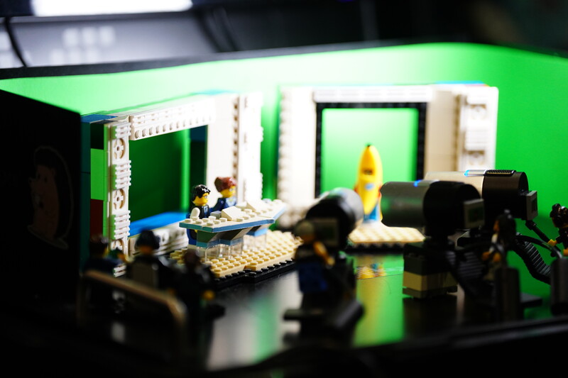 LEGO minifigures and set pieces on a green surface with camera equipment in foreground.
