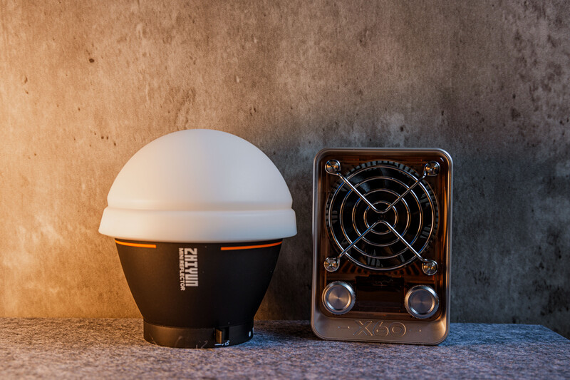 Two lighting tools on a textured surface: a dome-shaped LED light with black base and white diffuser, and a portable radio speaker with circular vents.