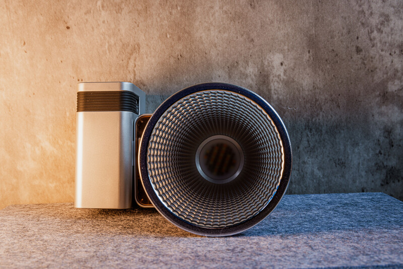 A cylindrical thermos bottle with brown and white bands positioned next to a round reflector with ribbed texture on weathered concrete surface.