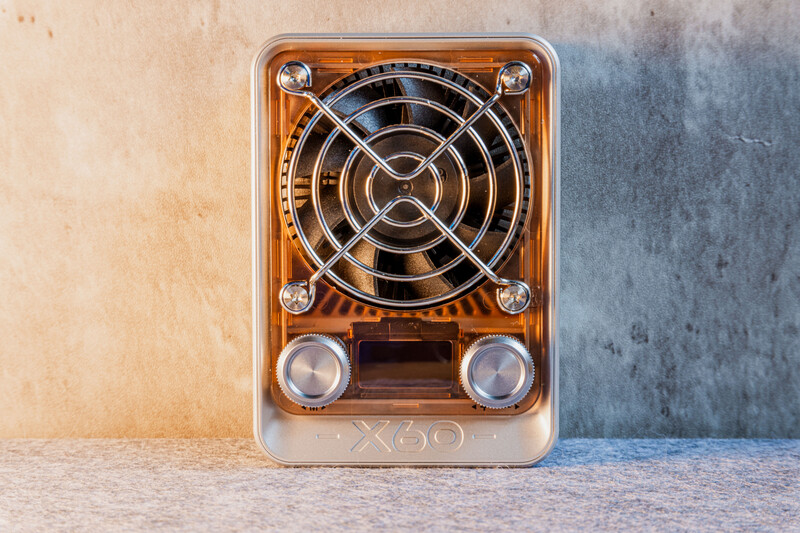 Transparent orange and white portable device with circular fan grille, two speaker elements, and model number visible on front.