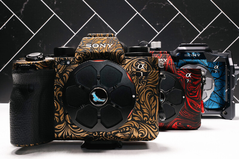 Collection of customized compact cameras with ornate decorative designs displayed against a herringbone tile backdrop.