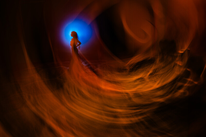 Figure silhouetted against bright blue light, surrounded by swirling orange and brown atmospheric layers.