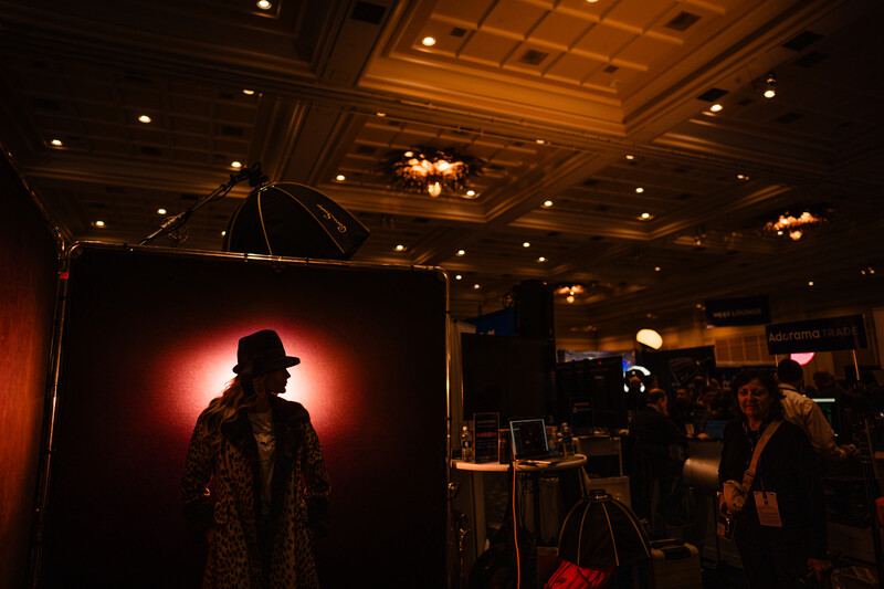 Silhouetted figure in fedora and patterned coat backlit by red-orange glow on dark stage.