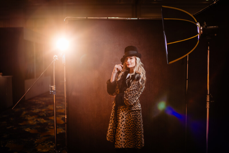 Woman in leopard coat and hat poses under dramatic studio lighting setup with large key light and reflector.