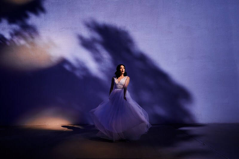 Woman in flowing lavender gown standing alone against dramatic purple-tinted mountainous backdrop with theatrical lighting.