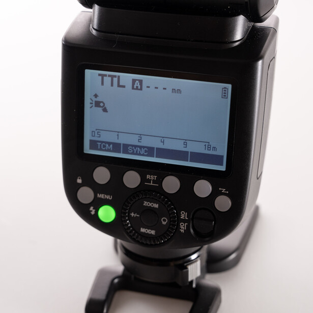 TTL flash unit with LCD screen displaying settings and control buttons on black background.