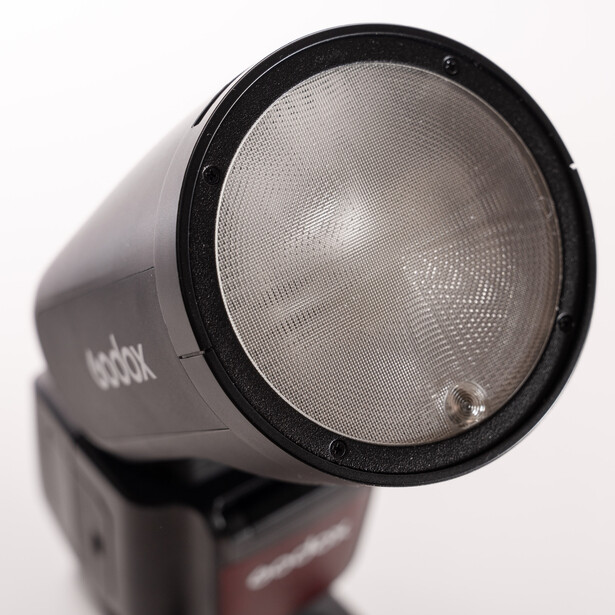 Close-up of a camera flash unit showing the reflector head and fresnel lens against a white background.