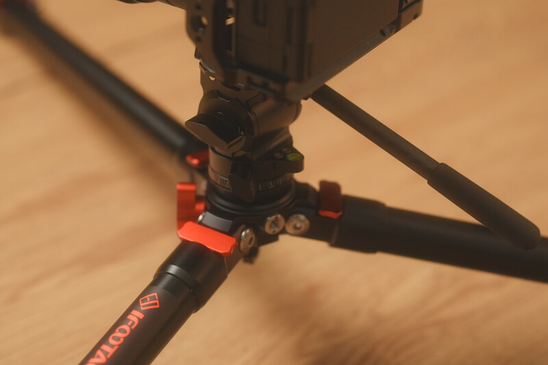 Close-up of a tripod head with red adjustment knobs and black ball mount on wooden surface.