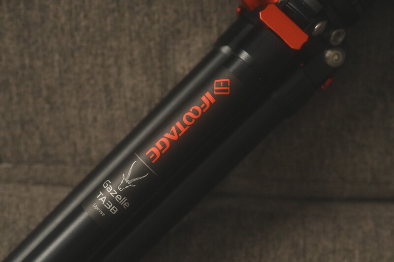 Close-up of a black camera seatpost with red accents and text markings against a neutral fabric background.