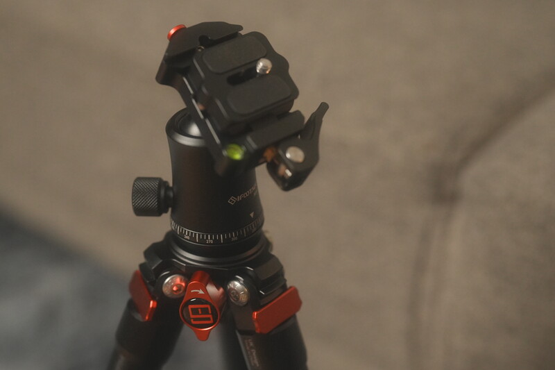 Black and red tripod head with fluid pan mechanism and bubble level, mounted on stand.