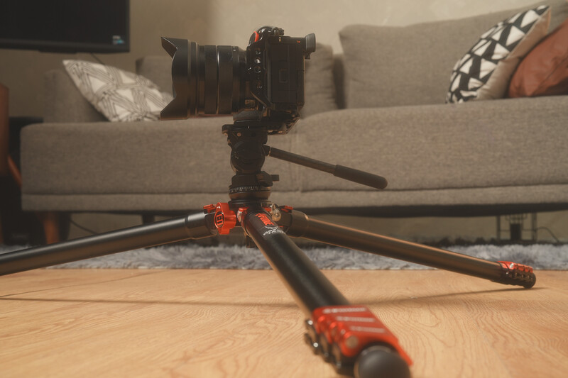 Professional camera mounted on red and black tripod with extended legs on wooden floor.