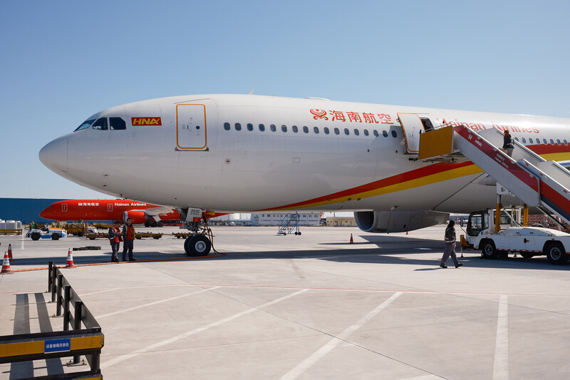 Wide-body commercial aircraft parked at airport terminal with boarding stairs and ground support vehicles.