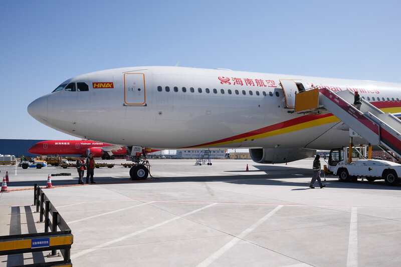 Commercial aircraft parked at airport gate with boarding stairs and ground service vehicles nearby.