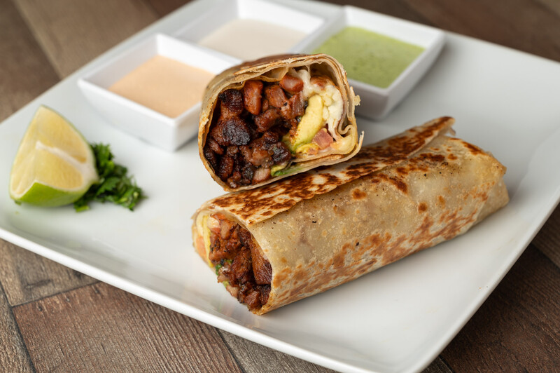 Two crispy wraps filled with meat and vegetables, one sliced in half to show the interior, served with lime wedge and three dipping sauces.