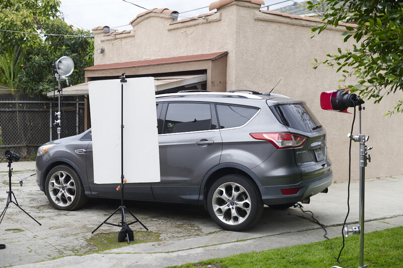 Gray SUV photographed outdoors with professional lighting setup including reflector panels and studio lights.