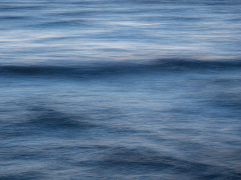 Ocean waves photographed with motion blur creating horizontal streaks of blue and white tones.