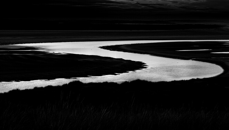 Winding river or stream cutting through dark landscape in high-contrast black and white.
