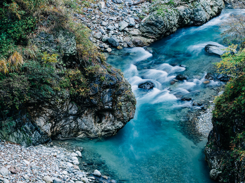 Turquoise river flowing through rocky canyon with moss-covered stone walls and vegetation.