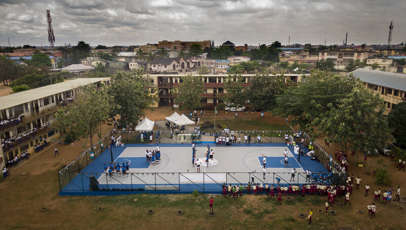 Aerial view of an outdoor athletic event on a blue platform surrounded by spectators in a school courtyard.