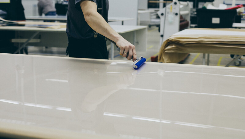 Worker applying blue tape to white surface panel in production facility.