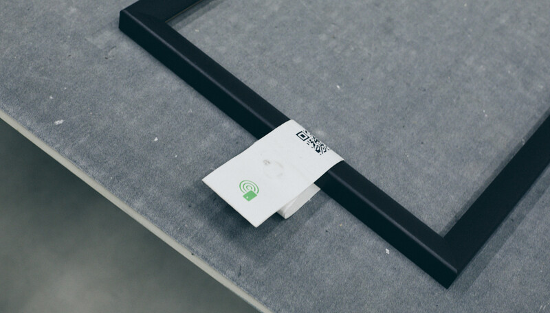 White wireless adapter with green indicator light placed on dark fabric surface next to black frame edge.
