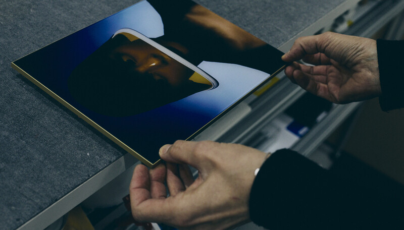 Photographer's hands holding an open portfolio book displaying a golden-toned landscape photograph against gray fabric.