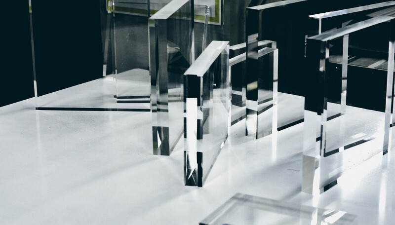 Architectural model with white geometric forms and black structural elements on a white base with dark background.