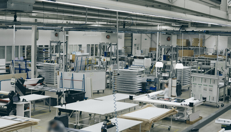 Industrial workshop with multiple workstations, materials, and manufacturing equipment organized throughout a bright, open space.