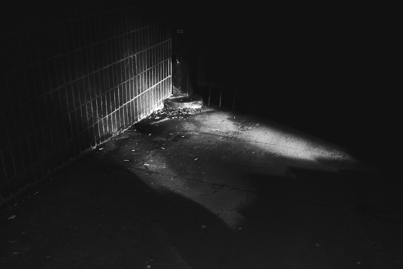 Metal gate in a dark concrete room illuminated by a single beam of light from above.