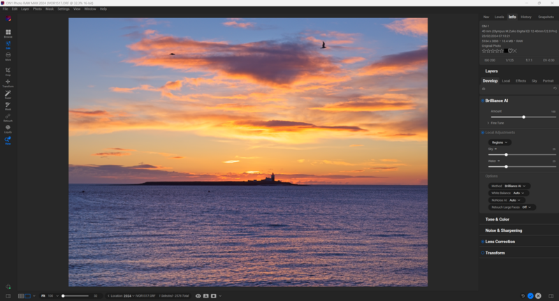 Dramatic sunset over calm ocean with silhouetted lighthouse on horizon beneath vibrant orange and purple clouds.