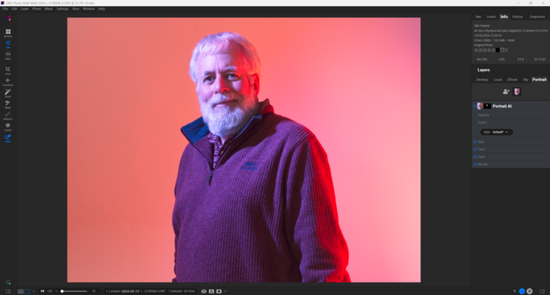 Older man with gray beard wearing purple zip-up sweater against coral-to-pink gradient background.