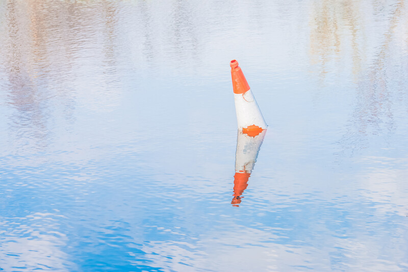 Orange and white buoy floating vertically in calm blue water with reflective surface.