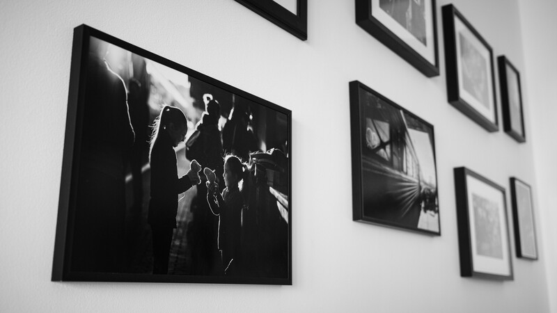 Black and white framed photographs arranged on a white wall, featuring a large portrait of a musician with a guitar on the left.