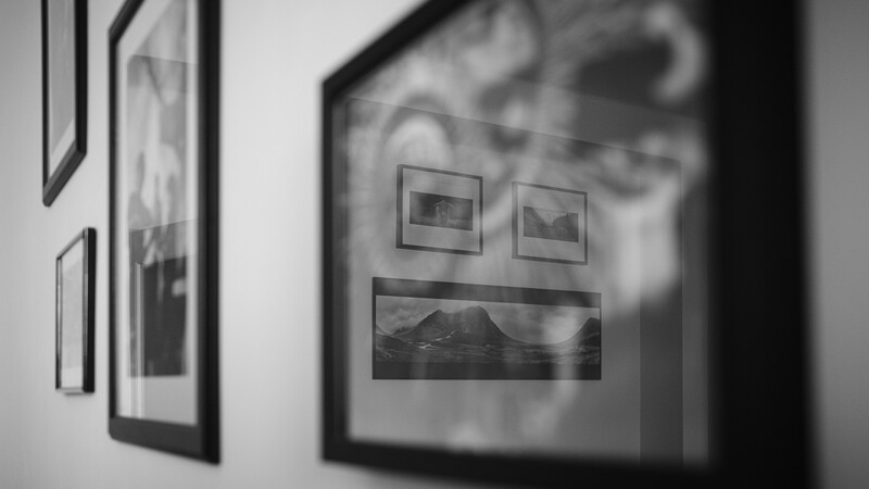 Black and white photograph of framed landscape images displayed on a gallery wall, shot at an angle with shallow depth of field.