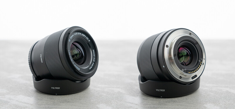 Two camera lenses with lens hoods displayed side by side on a gray surface.