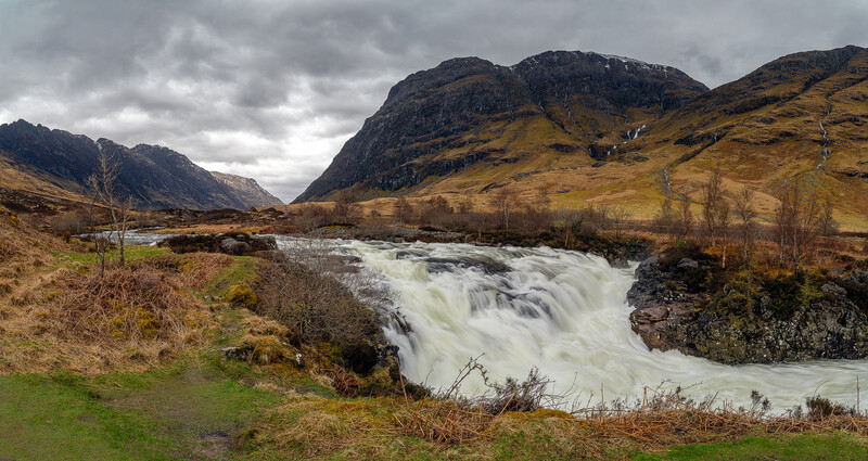 Waterfall cascading through moorland valley with mountains and dramatic cloudy sky.