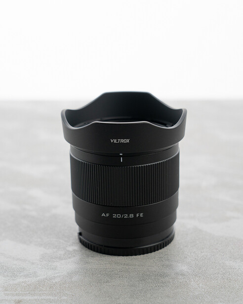 Viltrox 20mm f/2.8 ultra-wide lens with lens hood attached, displayed on concrete surface.