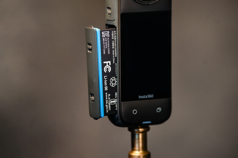Insta360 action camera mounted on a tripod ball head with brass connector against neutral background.