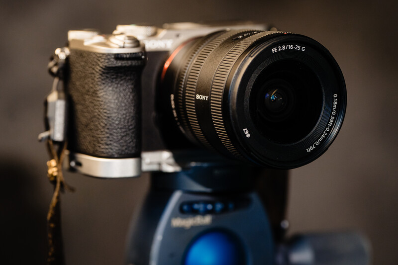 Sony mirrorless camera with attached telephoto lens on a blue ball head tripod mount.