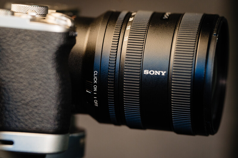 Sony mirrorless camera with attached telephoto lens featuring blue accent rings and distance markings.