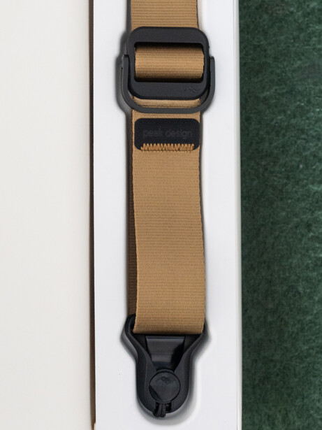 Tan and black camera strap with plastic adjustment buckle and clip attachment.