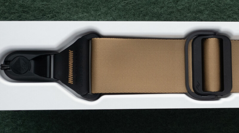 Tan fabric strap with black plastic hardware and adjustment buckles on white background.