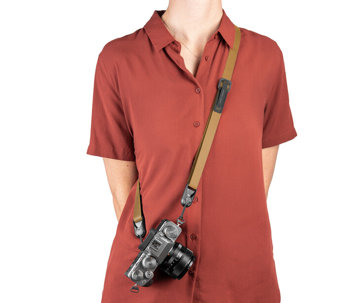 Person wearing rust-colored button-up shirt with vintage rangefinder camera suspended on tan leather strap.