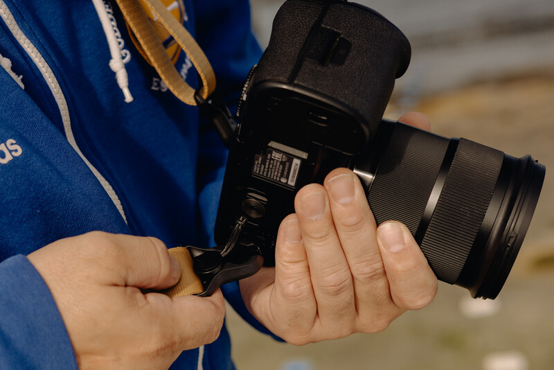 Photographer holding a black mirrorless camera with telephoto lens while wearing a blue jacket.
