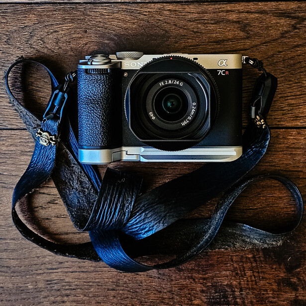 Compact rangefinder camera with black body and blue-striped camera strap on wooden surface.