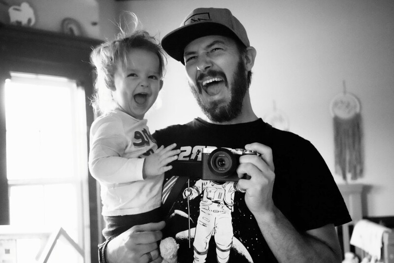 Man holding a camera and smiling child in black and white portrait.
