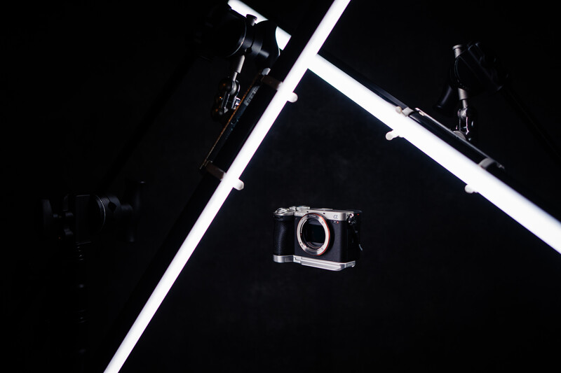 Camera suspended in mid-air between two white horizontal bars against a black background.