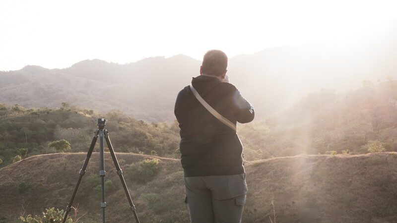 Photographer with camera on tripod overlooking misty mountain landscape at golden hour.