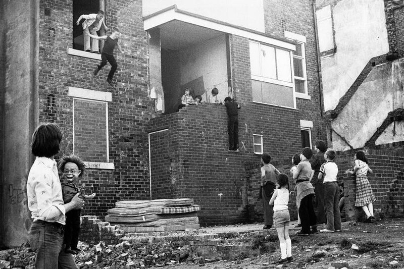 Children gathered in a brick courtyard watching performers on an elevated platform.